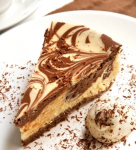 Chocolate marble cheesecake with cream and shaved chocolate, and a cup of coffee.